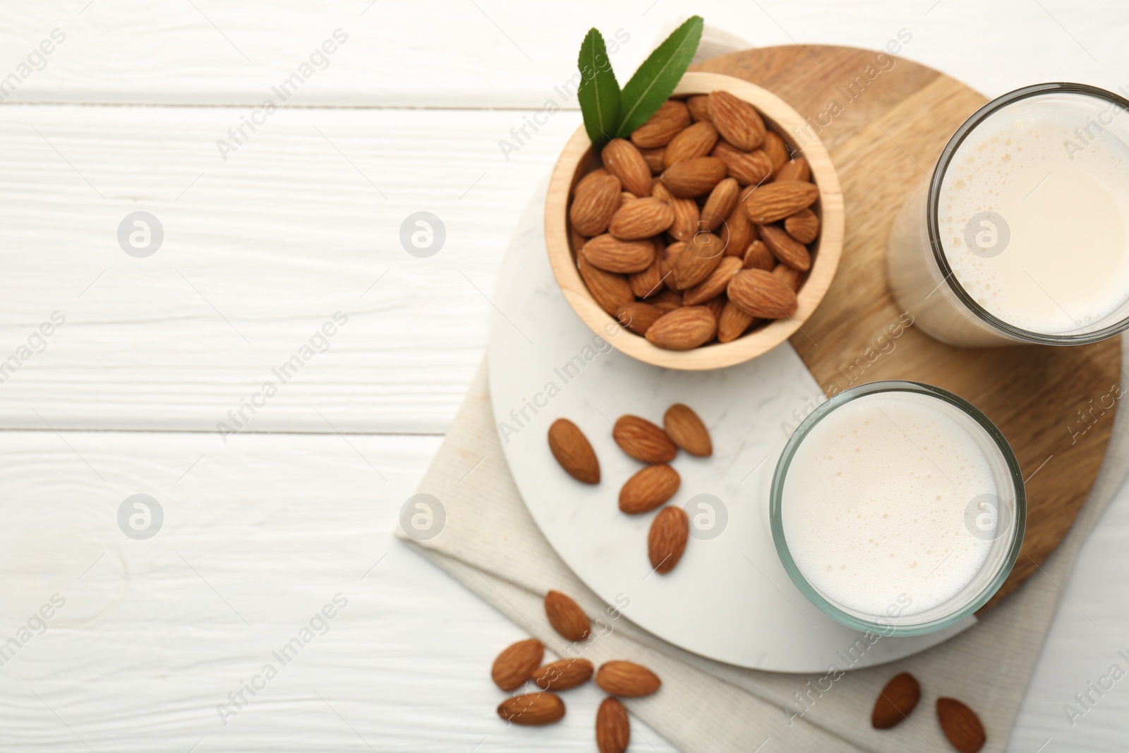 Photo of Glasses of almond milk and almonds on white wooden table, top view. Space for text