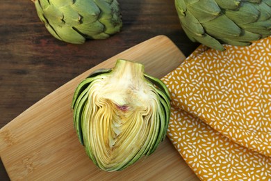 Photo of Whole and cut fresh raw artichokes on wooden table, flat lay