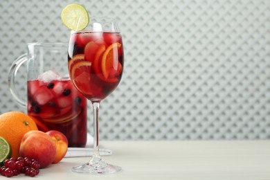 Photo of Glass and jug of Red Sangria with fruits on white wooden table, space for text