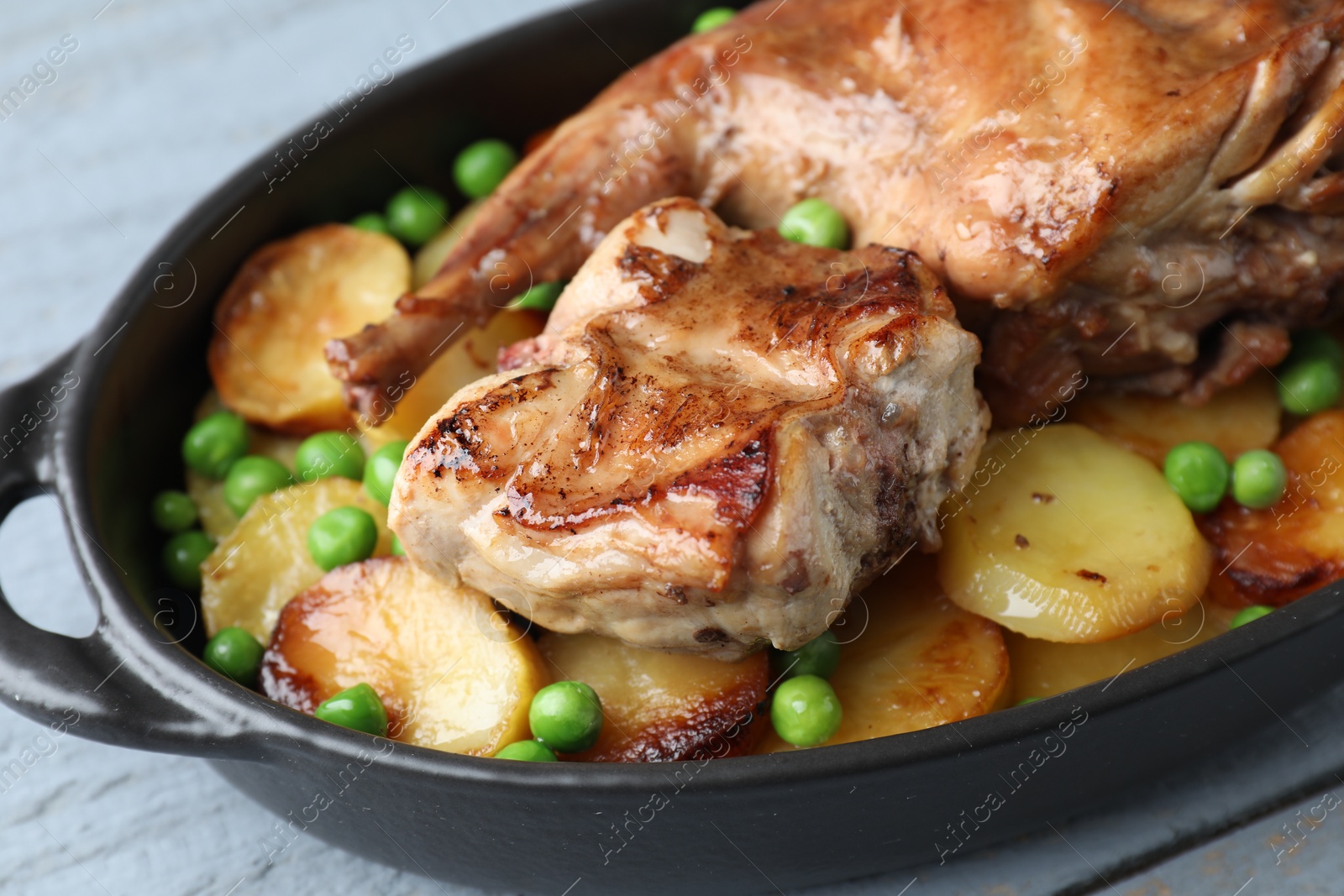 Photo of Tasty cooked rabbit with vegetables in baking dish on grey table, closeup