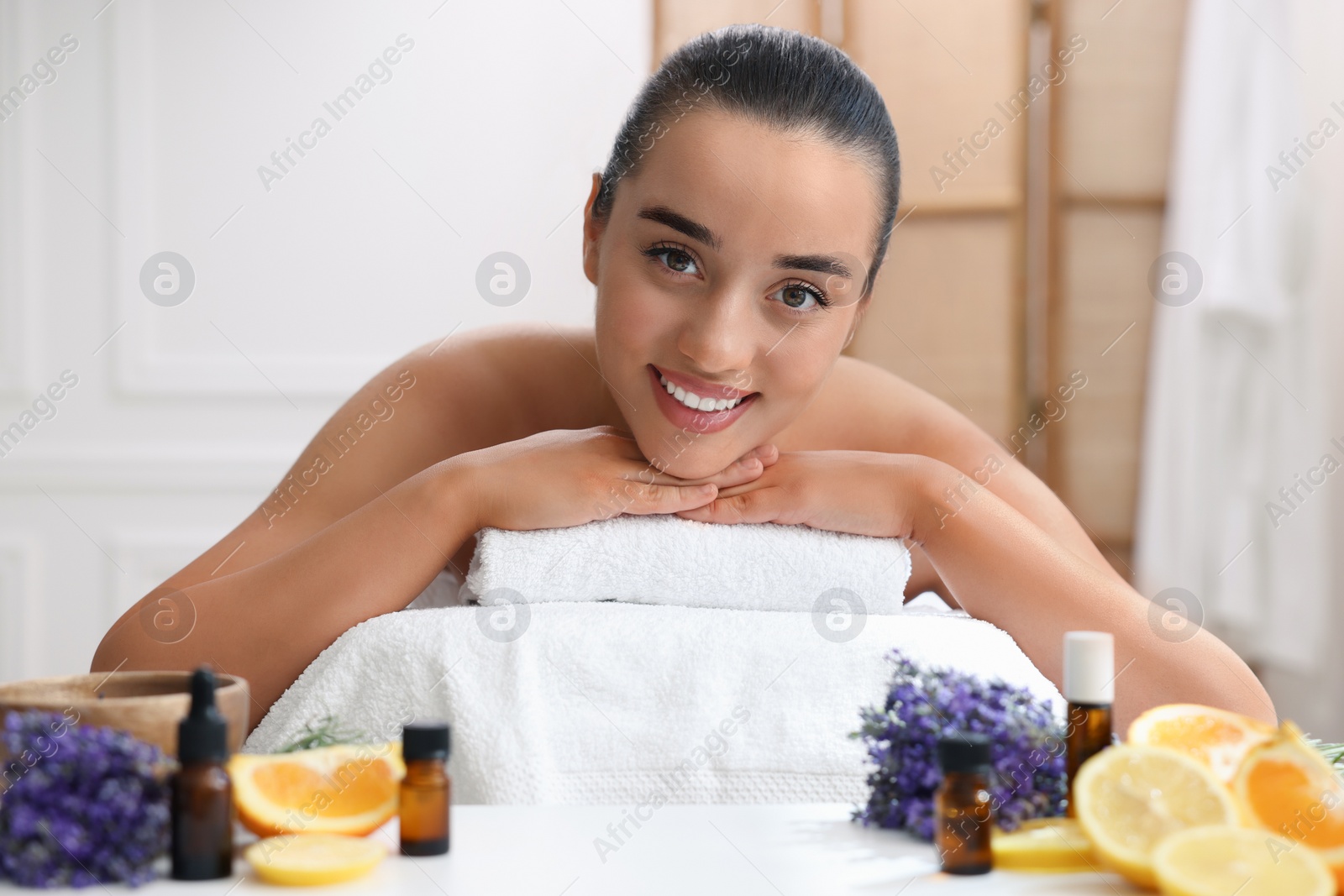 Photo of Beautiful young woman relaxing on massage couch and bottles of essential oil with ingredients on table in spa salon