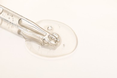 Photo of Glass pipette and transparent liquid on beige background, closeup. Space for text