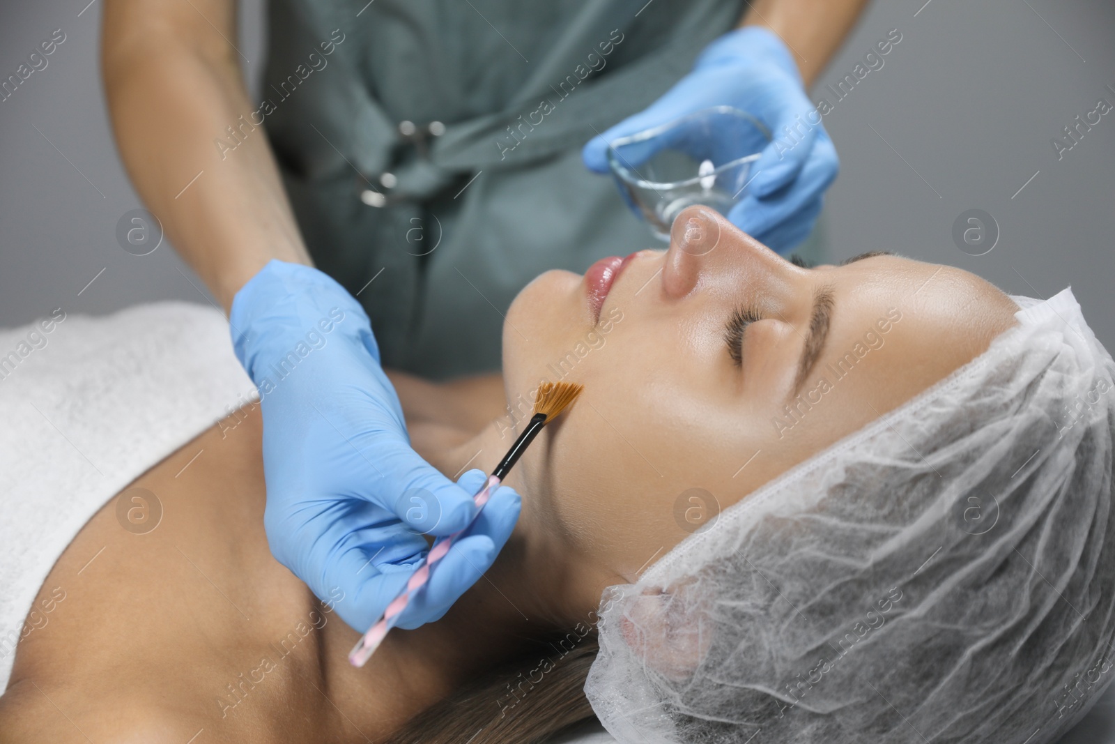 Photo of Cosmetologist applying chemical peel product on client's face in salon