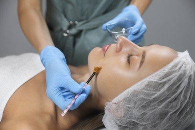 Photo of Cosmetologist applying chemical peel product on client's face in salon