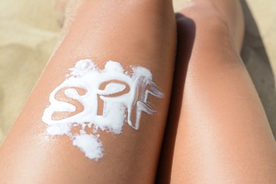Photo of Woman with abbreviation SPF of sunscreen on leg at beach, closeup