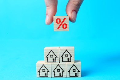Image of Mortgage rate. Woman building pyramid of cubes with percent sign and house icons on light blue background, closeup