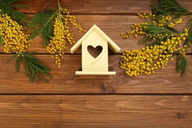 Photo of Stylish bird house and fresh mimosas on wooden background, flat lay. Space for text