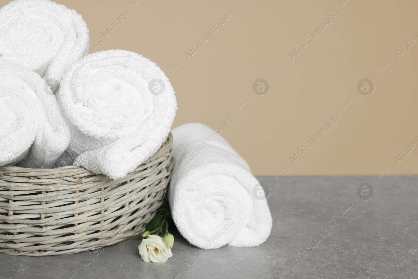 Photo of Soft rolled towels in wicker basket on grey table, space for text