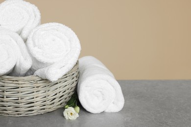 Soft rolled towels in wicker basket on grey table, space for text