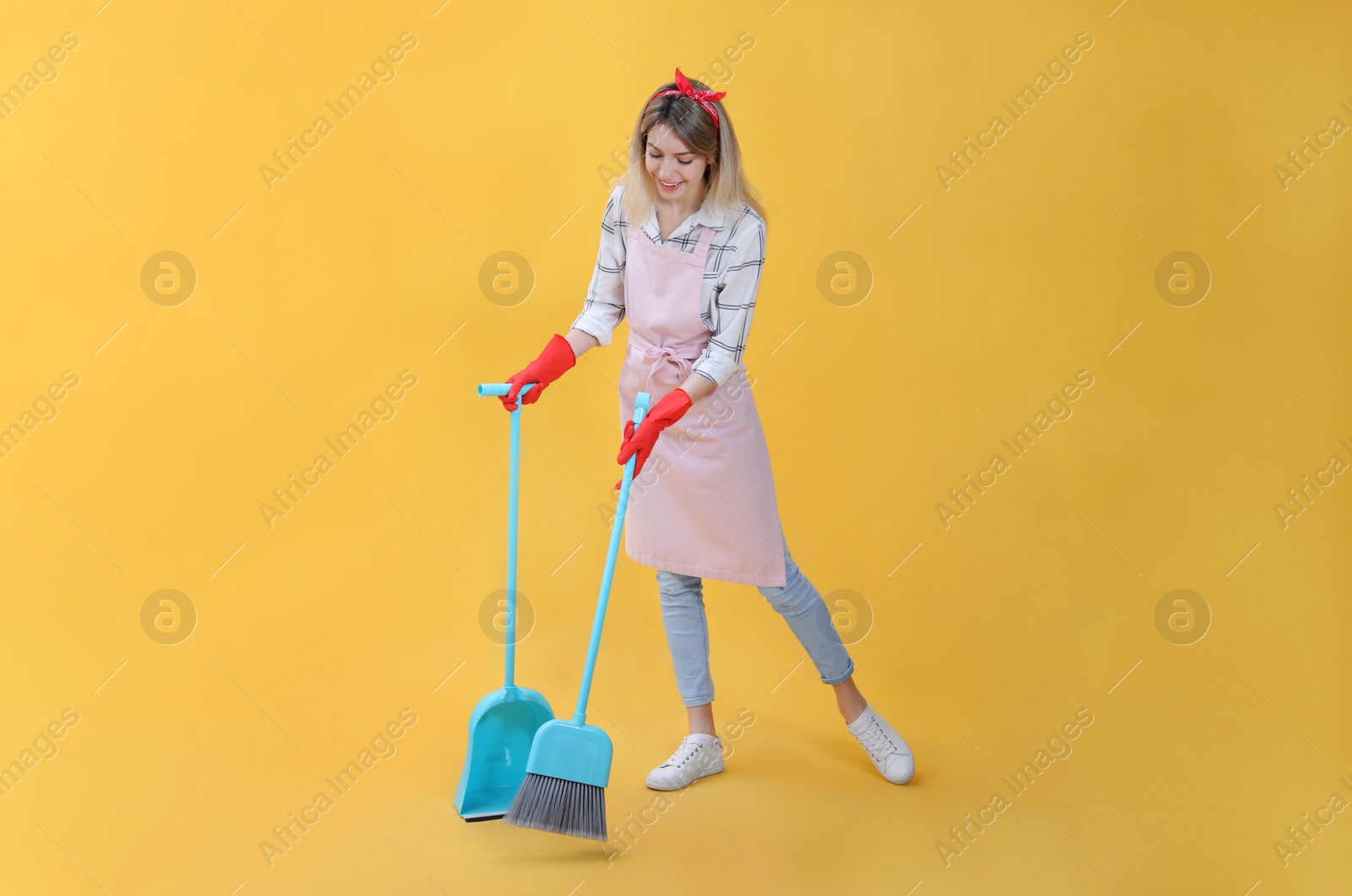 Photo of Young housewife with broom and dustpan on yellow background