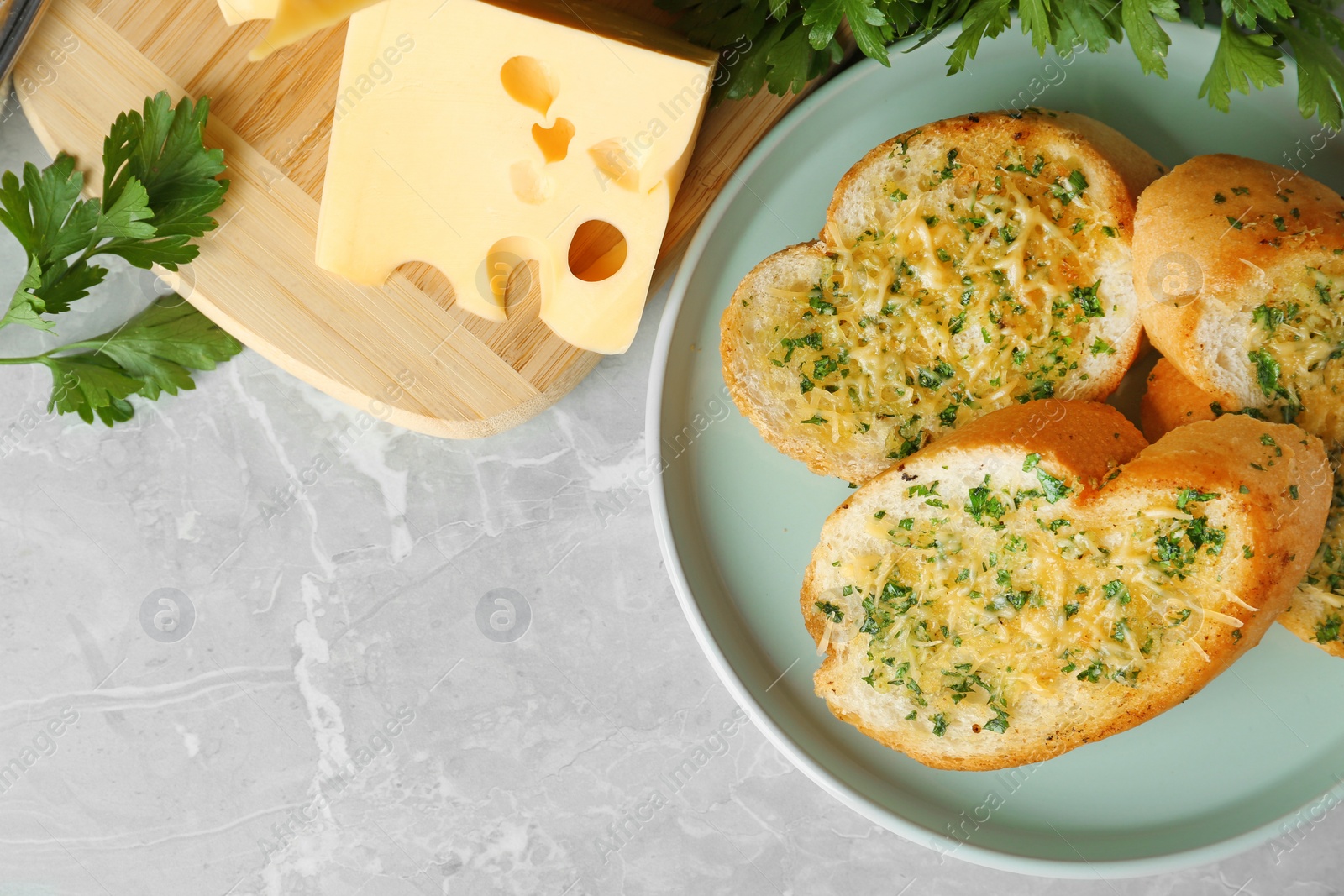 Photo of Slices of toasted bread with garlic, cheese and herbs on grey table, flat lay. Space for text