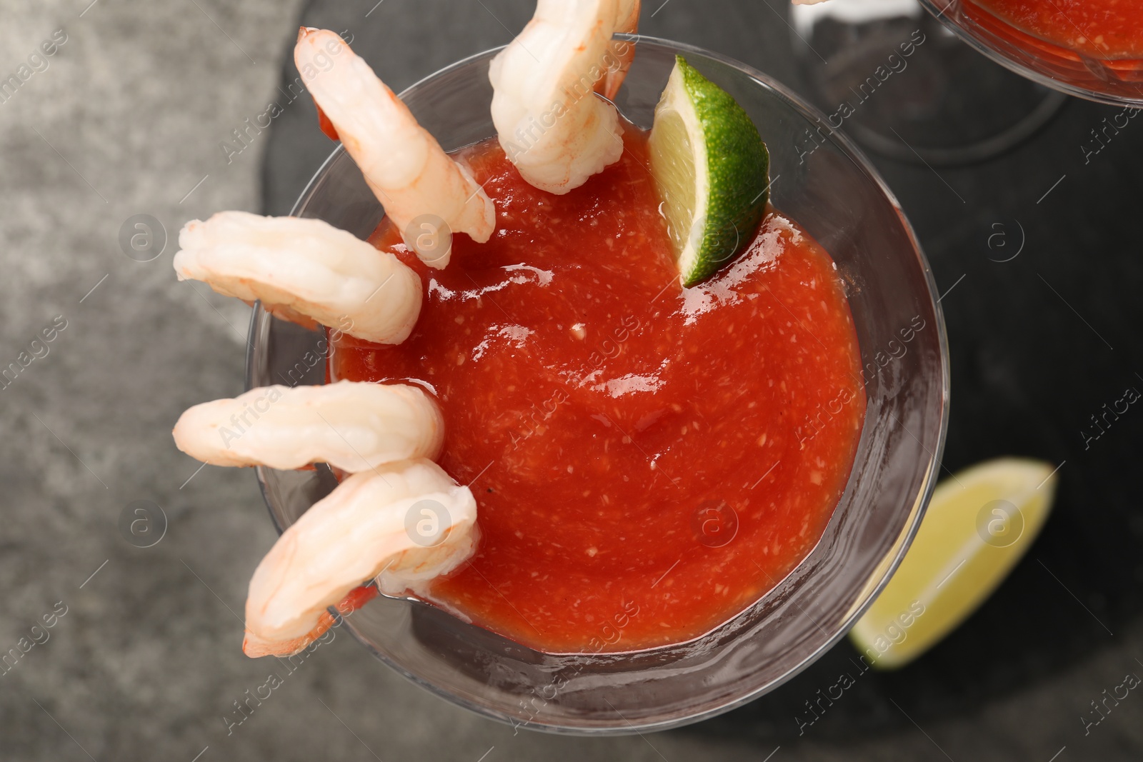 Photo of Tasty shrimp cocktail with sauce in glasses and lime on grey table, top view