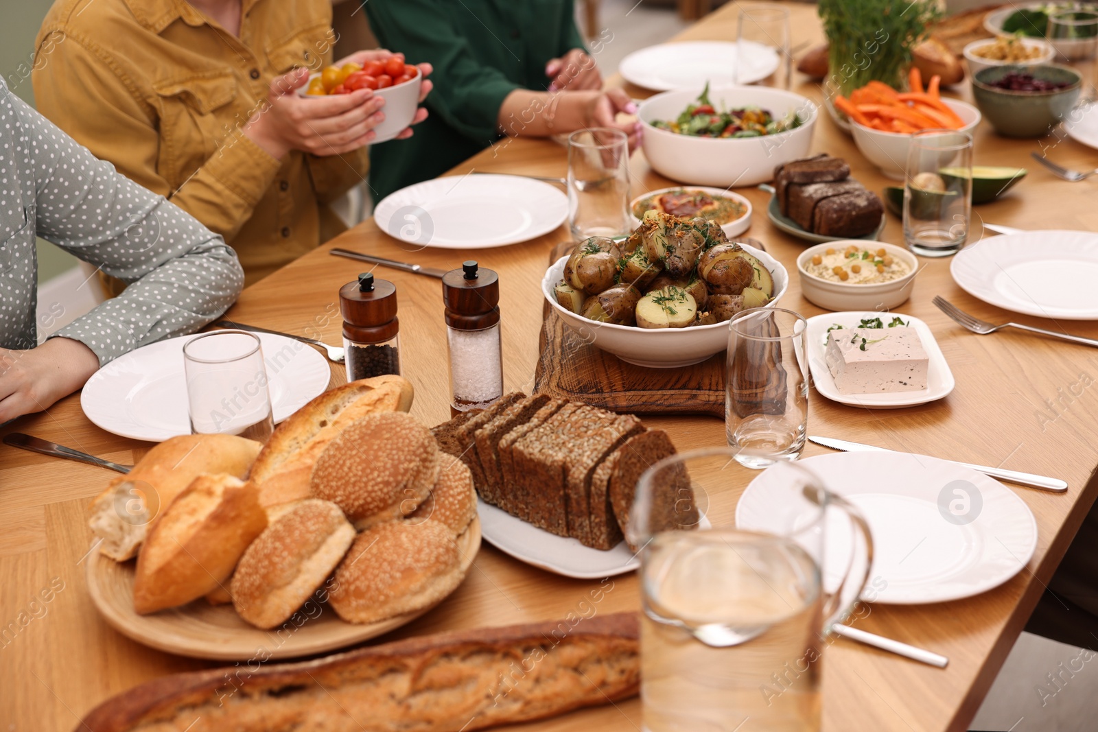 Photo of Friends eating vegetarian food at wooden table indoors, closeup