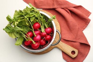 Wet radish in colander on white table, top view