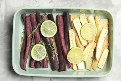 Photo of Raw black and white carrots with lime slices in baking dish on light grey table, top view