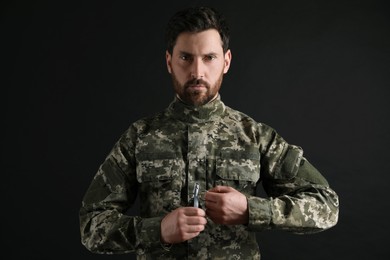 Soldier pulling safety pin out of hand grenade on black background. Military service