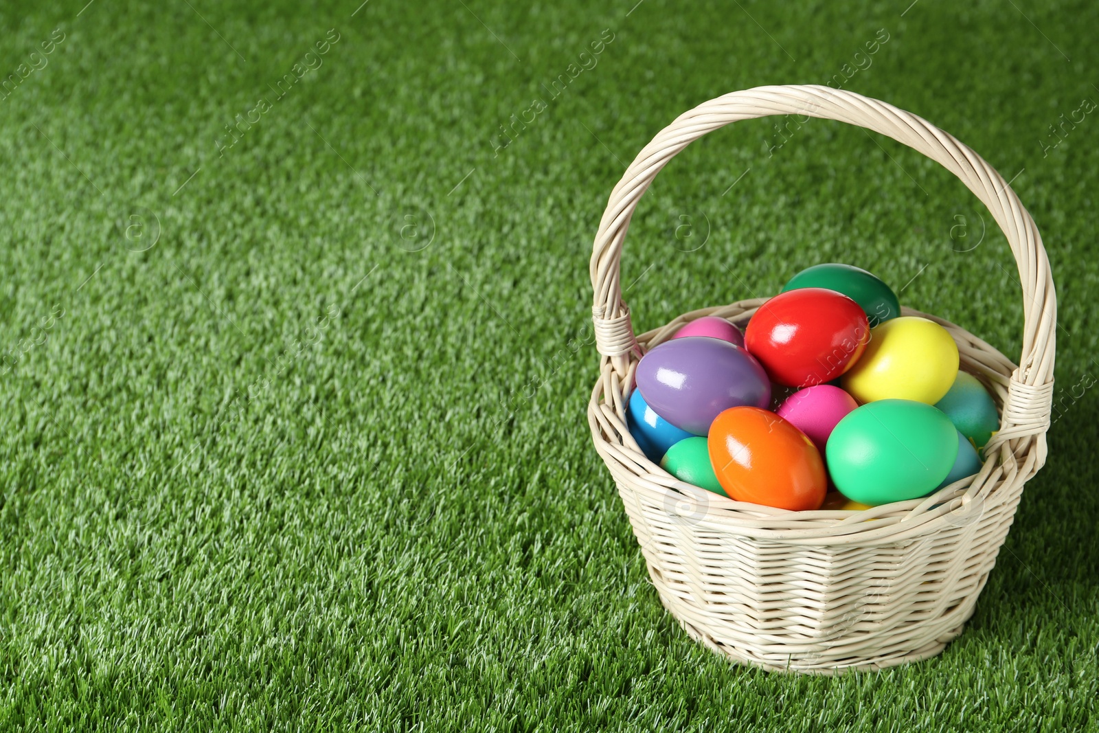 Photo of Wicker basket with Easter eggs on green grass. Space for text