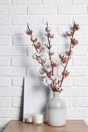 Photo of Cotton branches with fluffy flowers in vase on wooden table near white brick wall