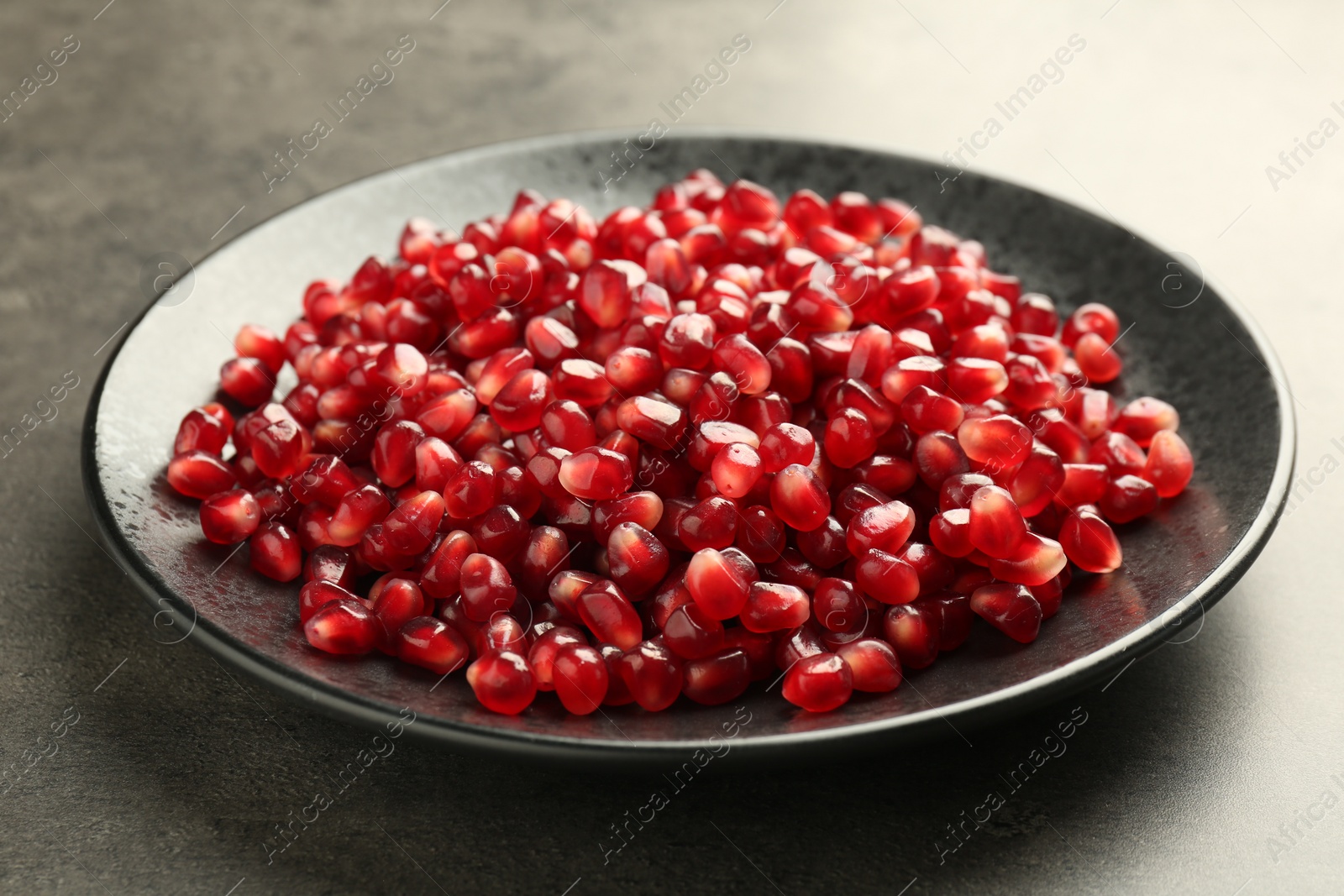 Photo of Ripe juicy pomegranate grains on grey table, closeup