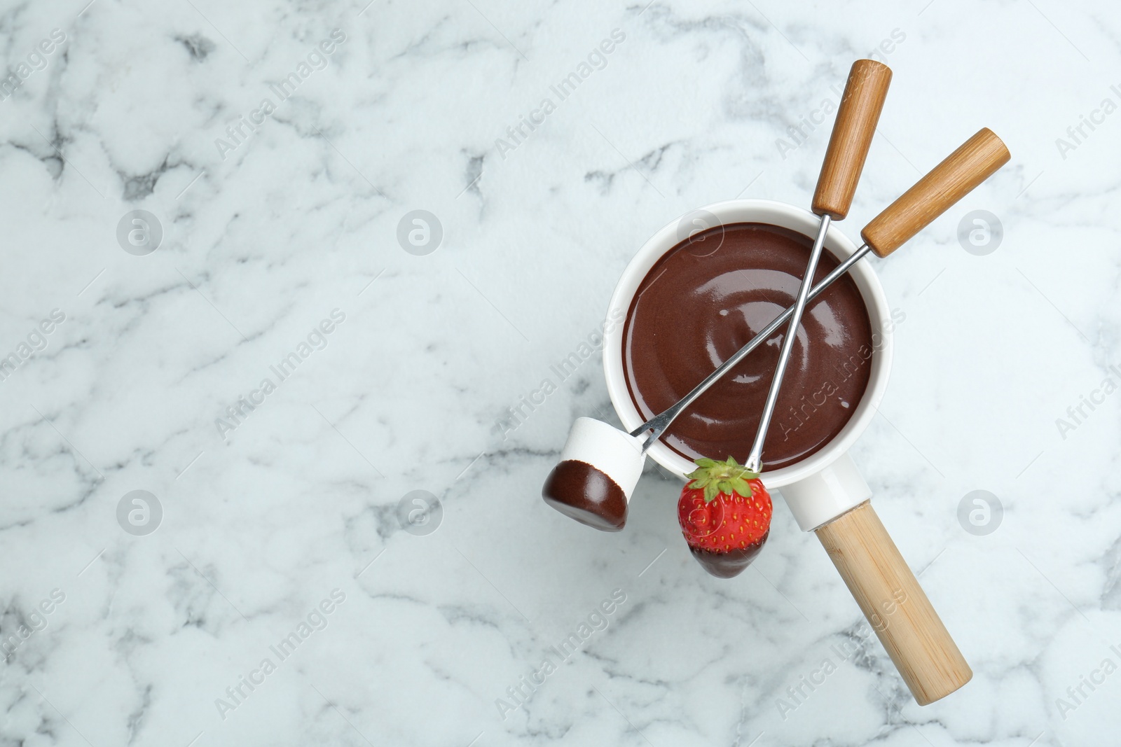 Photo of Fondue pot of melted chocolate, forks with sweet marshmallow and fresh strawberry on white marble table, flat lay. Space for text