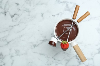 Photo of Fondue pot of melted chocolate, forks with sweet marshmallow and fresh strawberry on white marble table, flat lay. Space for text