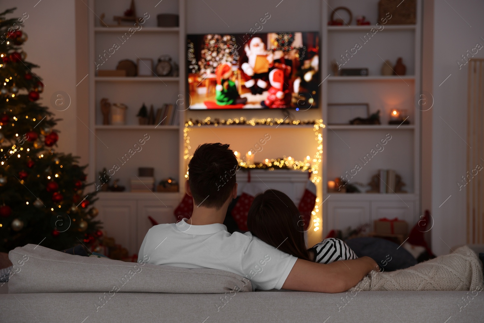 Photo of Couple watching Christmas movie via TV in cosy room, back view. Winter holidays atmosphere