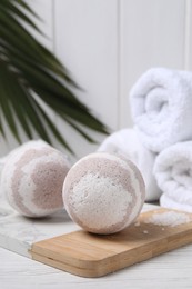 Photo of Bath bombs, sea salt and rolled towels on white wooden table, closeup