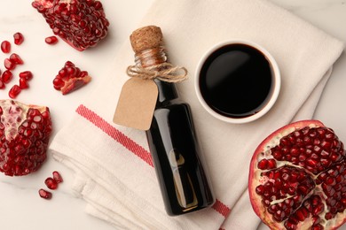 Photo of Bottle of pomegranate sauce and fresh ripe fruit on white marble table, flat lay