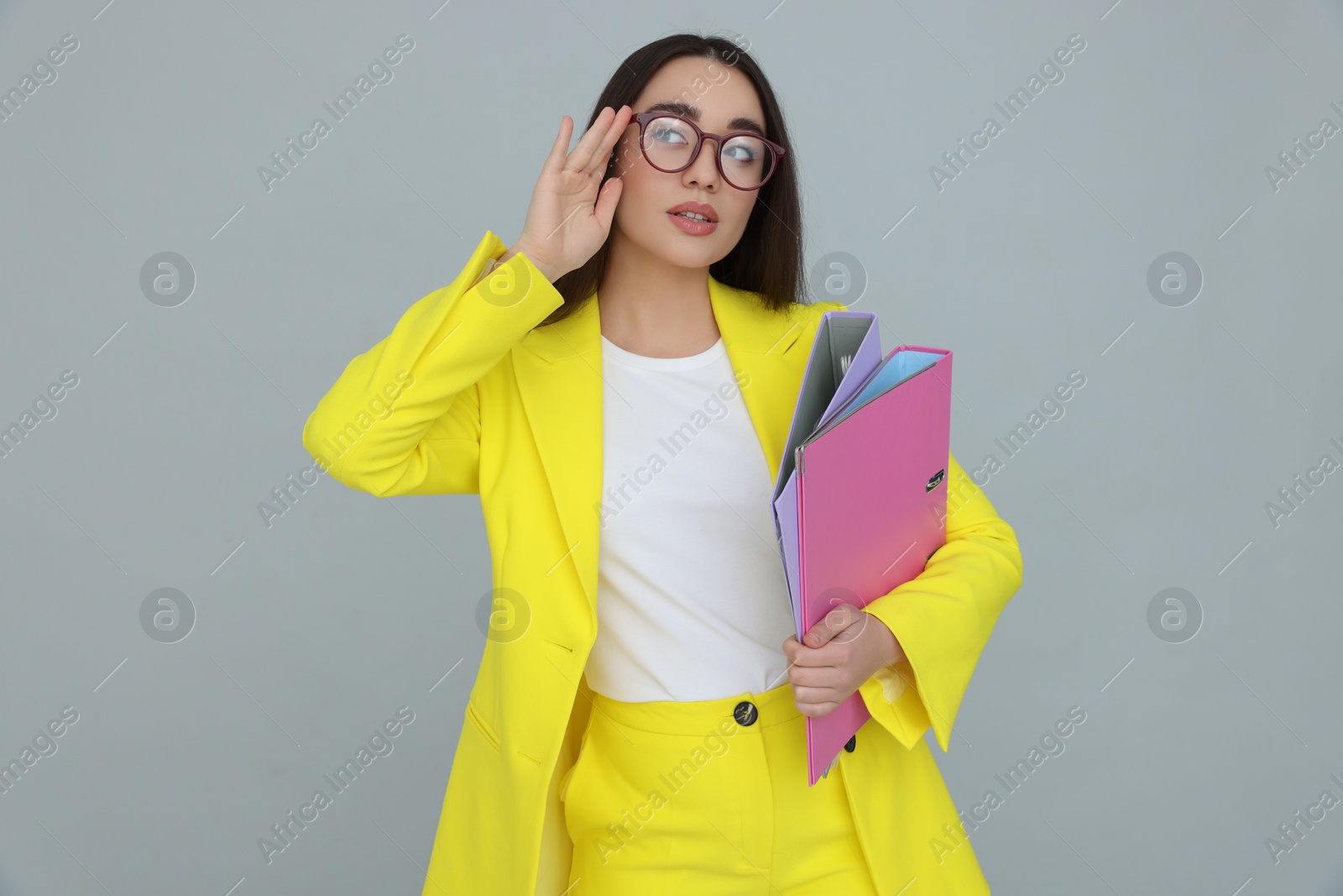 Photo of Young female intern with eyeglasses and folders on grey background