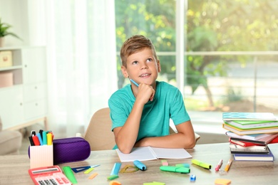 Photo of Cute boy doing homework at table with school stationery indoors