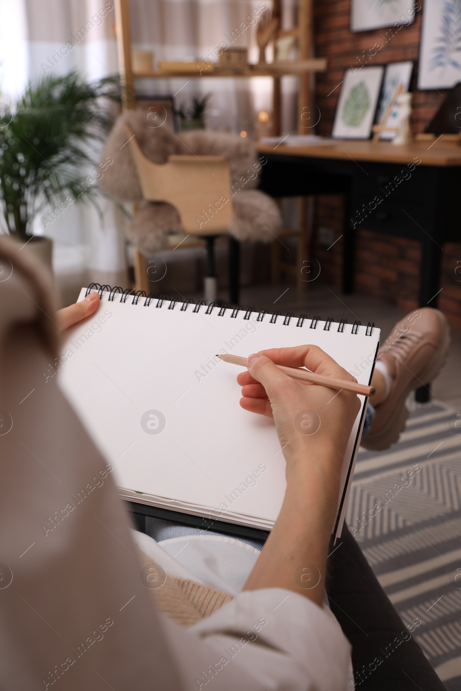 Photo of Woman drawing in sketchbook with pencil at home, closeup