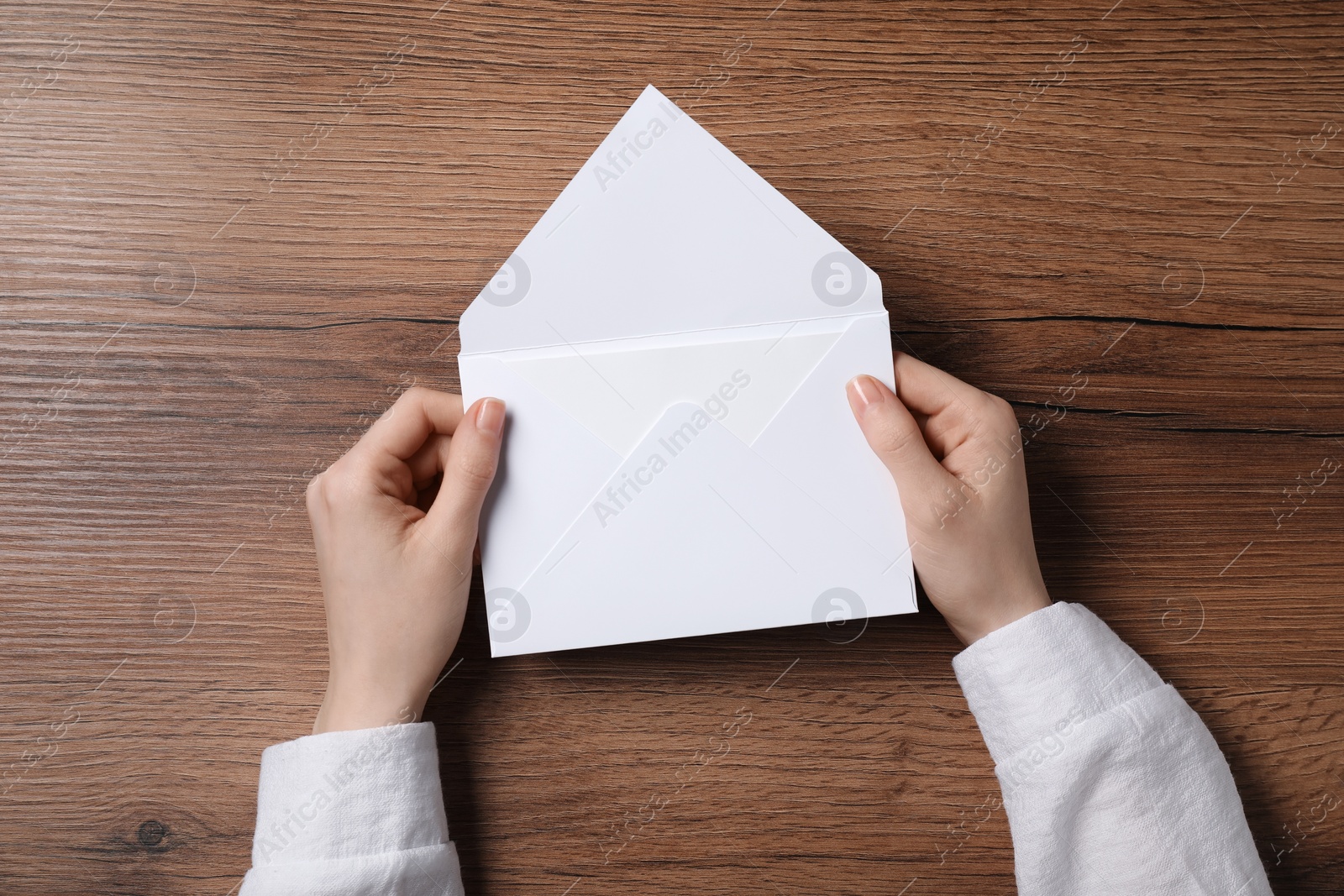 Photo of Woman holding letter envelope with card at wooden table, top view