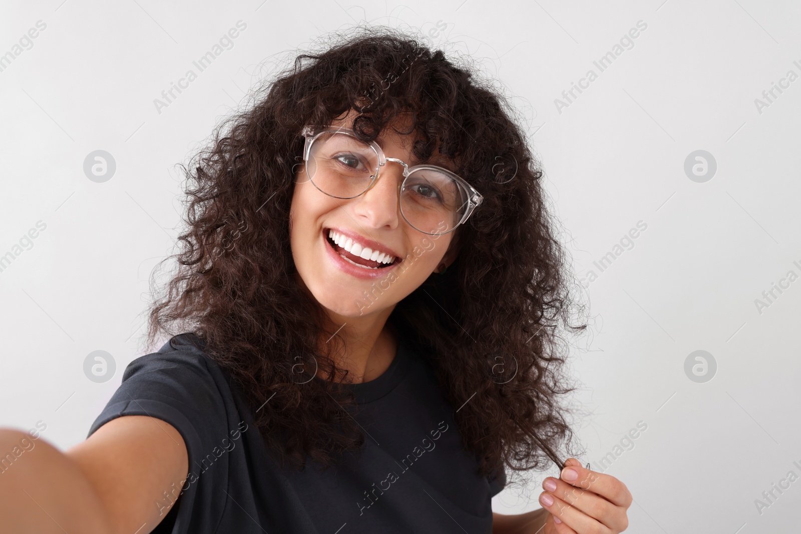 Photo of Beautiful young woman in eyeglasses taking selfie on light grey background