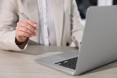 Woman with pen working on laptop at wooden table, closeup. Electronic document management