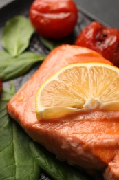 Photo of Tasty grilled salmon with lemon, spinach and tomatoes on table, closeup