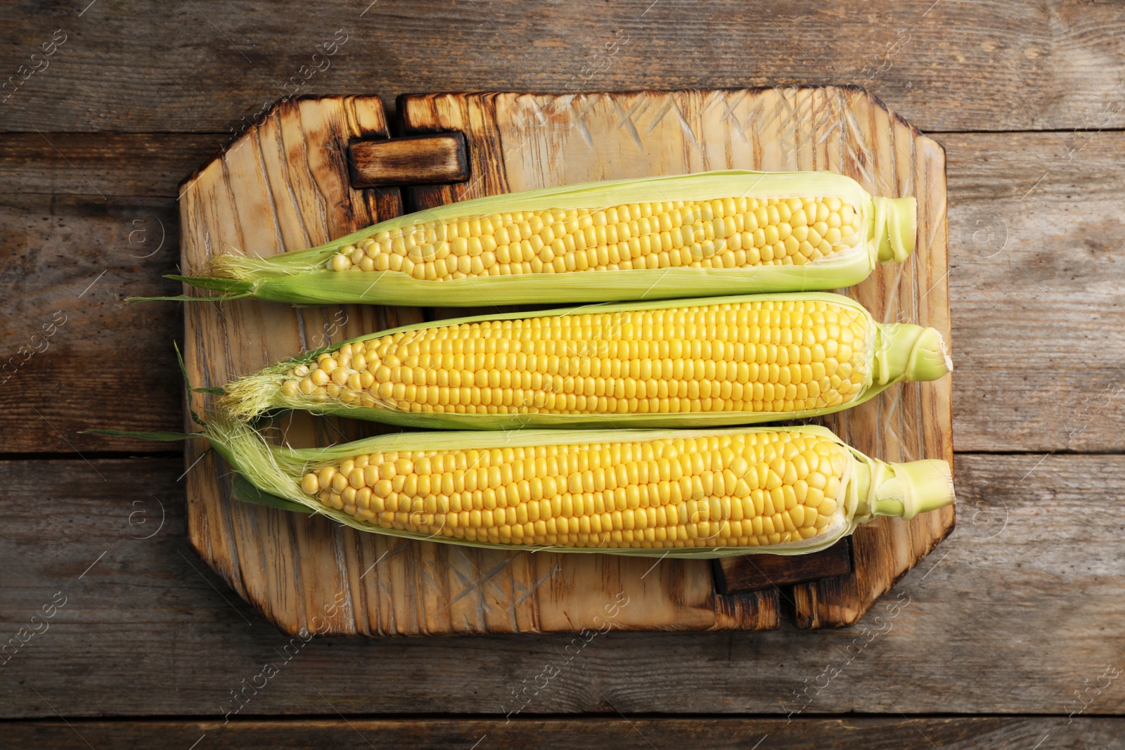 Photo of Tasty sweet corn cobs on wooden board, top view