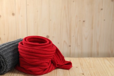 Photo of Red and gray knitted scarfs on wooden table, space for text