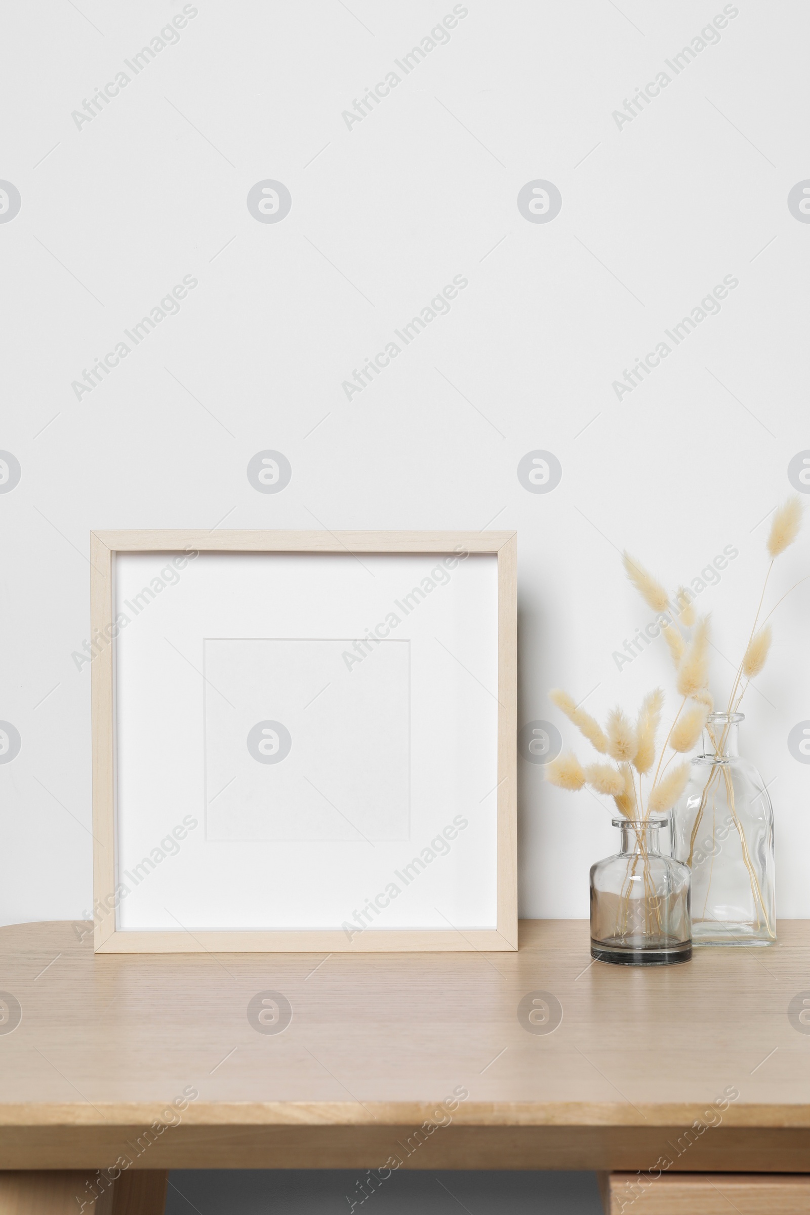 Photo of Empty photo frame and vases with dry decorative spikes on wooden table. Mockup for design