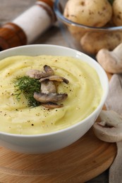 Photo of Bowl of tasty cream soup with mushrooms, dill and raw potatoes on wooden table, closeup