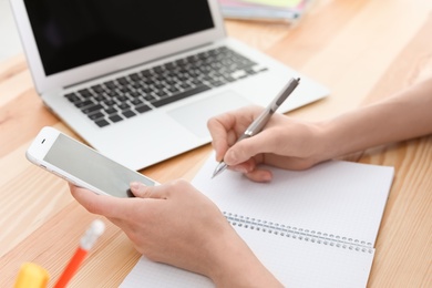 Photo of Young woman working with mobile phone and laptop at desk. Home office