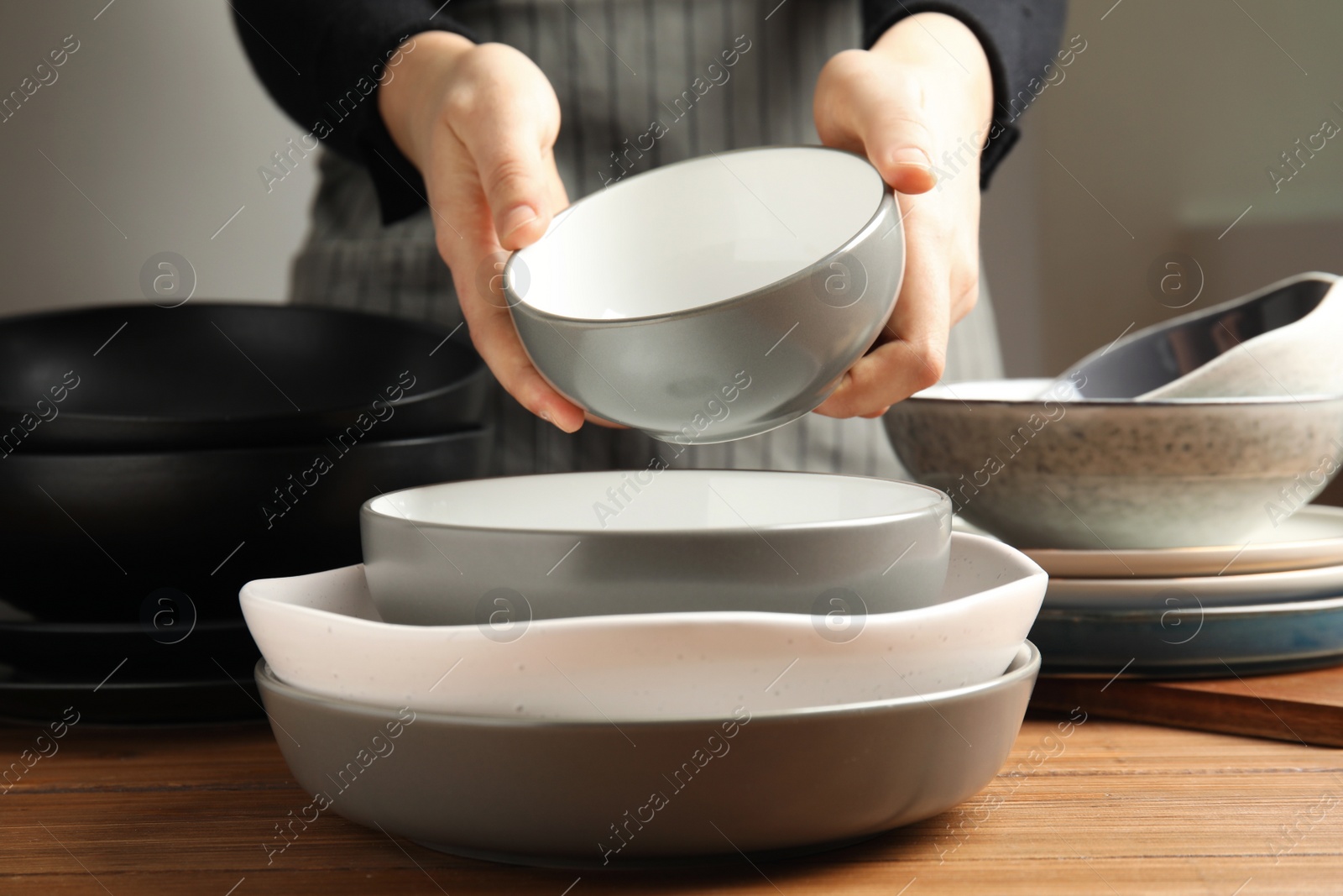 Photo of Woman holding bowl over clean dishware, closeup