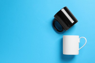 Photo of White and black ceramic mugs on light blue background, flat lay. Space for text