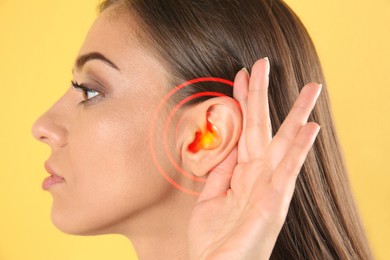 Image of Young woman with hearing problem on yellow background, closeup