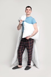 Photo of Happy man in pyjama with blanket and pillow on light grey background