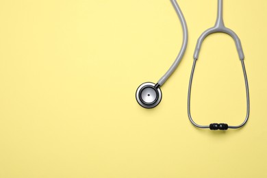 Stethoscope on yellow background, top view. Space for text