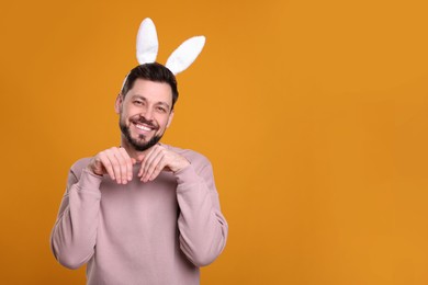Photo of Happy man wearing bunny ears headband on orange background, space for text. Easter celebration