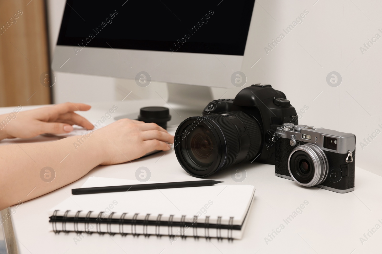 Photo of Photographer working on computer at white table with cameras indoors, closeup