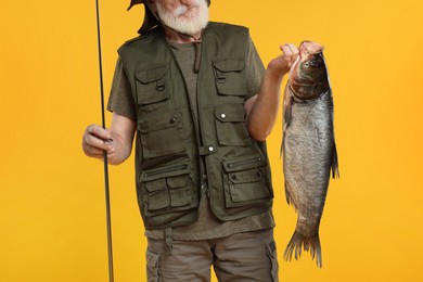 Photo of Fisherman with rod and catch on yellow background, closeup
