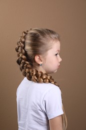 Photo of Little girl with braided hair on light brown background