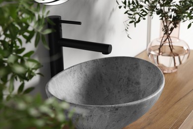 Photo of Eucalyptus branches near vessel sink on bathroom vanity. Interior design